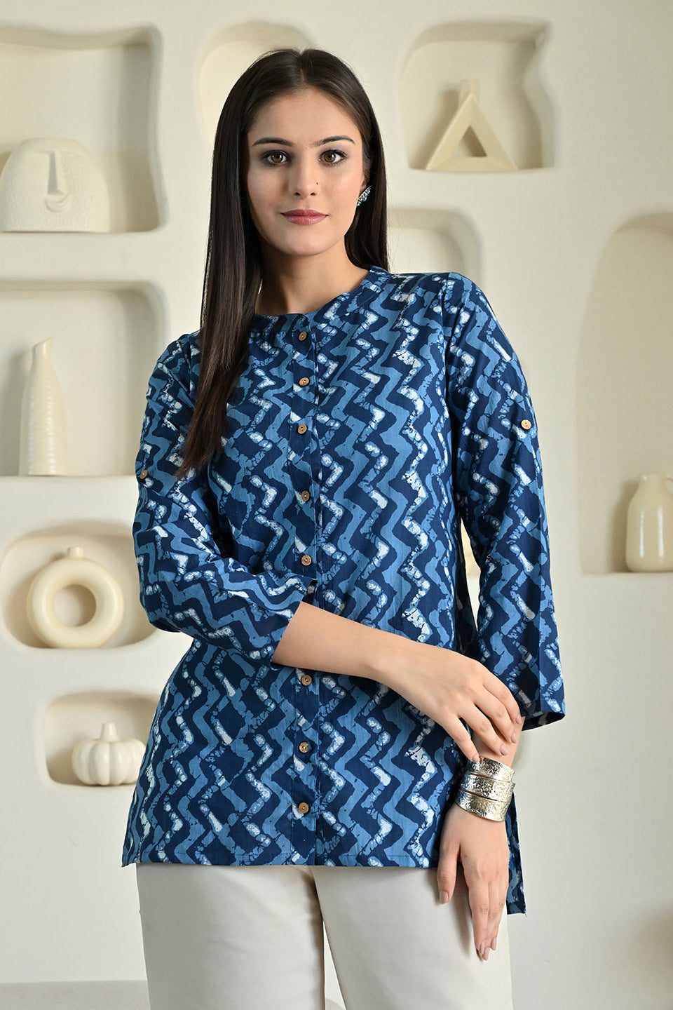 Woman wearing a blue patterned shirt from Desi Tassels in front of a decorative wall.
