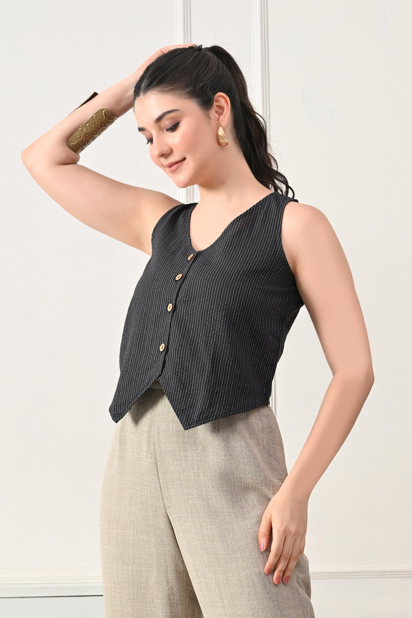 Woman wearing a black sleeveless top with buttons from Desi Tassels and beige pants against a white background