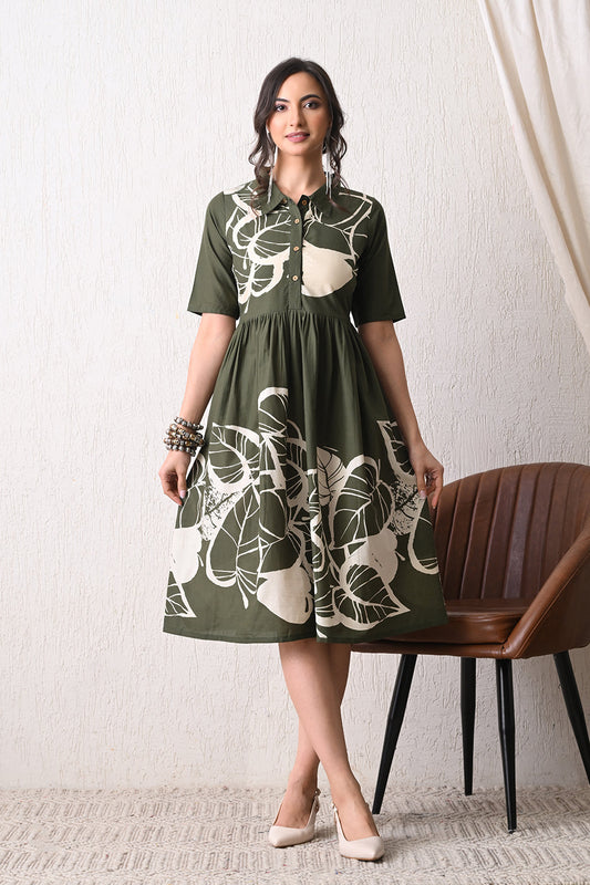 Woman wearing a green dress with white floral pattern from Desi Tassels standing in a room with a chair and white wall.