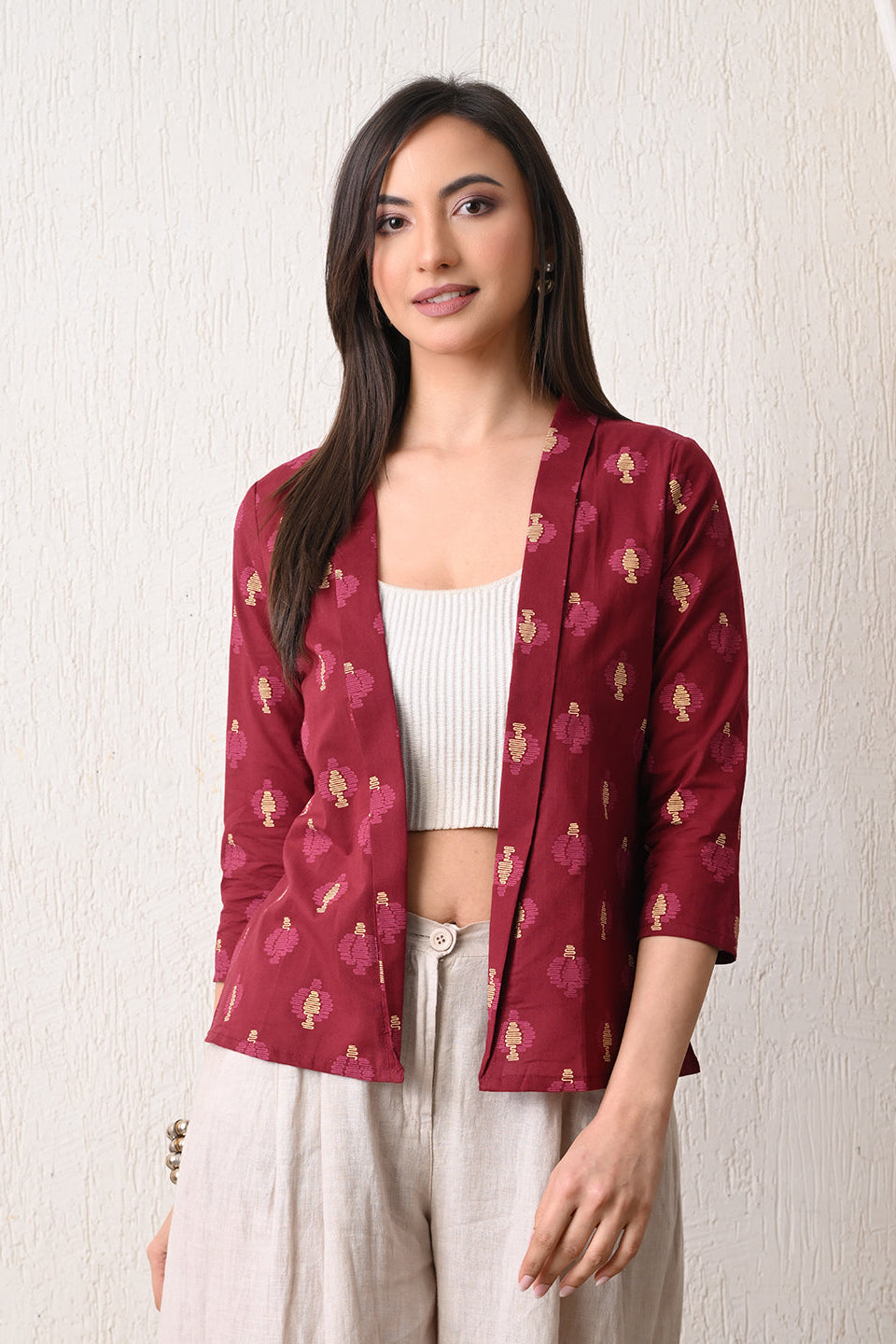 Woman wearing a maroon patterned jacket from Desi Tassels over a white top and light pants on a plain background