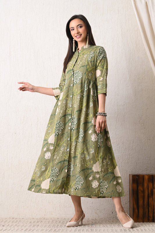 Woman wearing a green floral dress from Desi Tassels against a white wall.