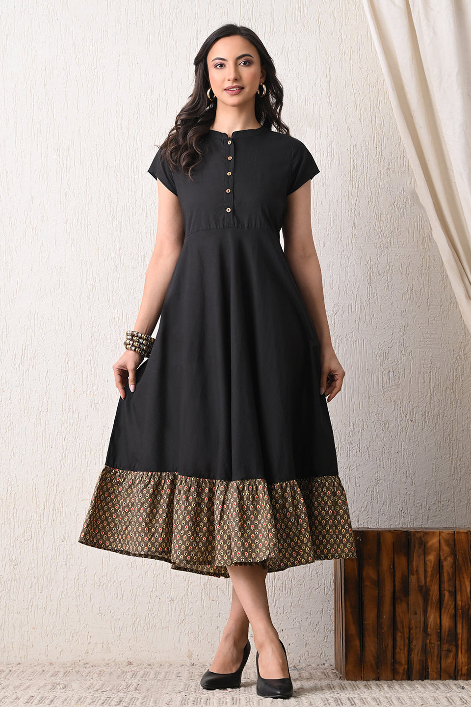 Woman wearing a black dress with a patterned hem from Desi Tassels against a white wall.