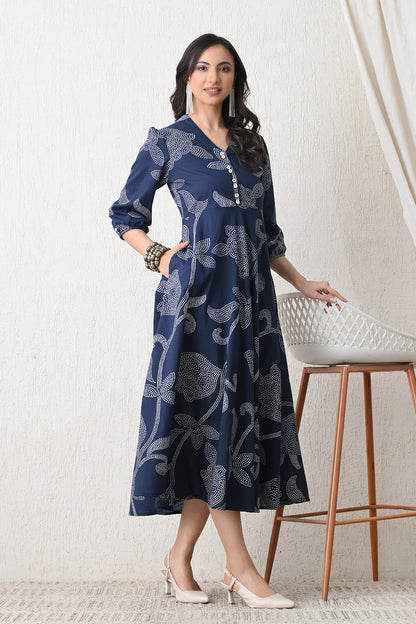 Woman wearing a blue patterned dress from Desi Tassels standing in a room with a white stool.