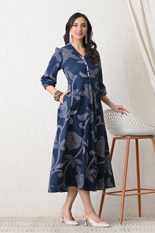 Woman wearing a blue patterned dress from Desi Tassels standing in a room with a white stool.