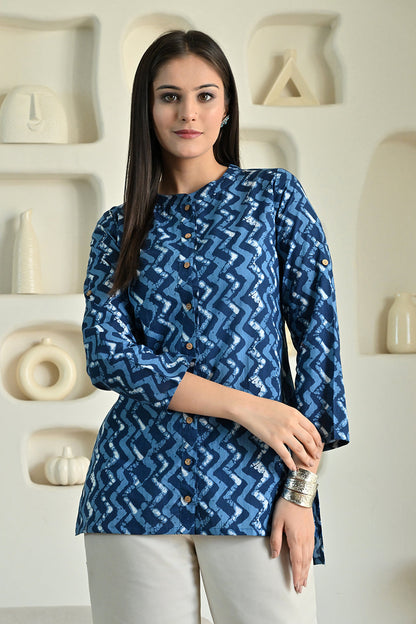 Woman wearing a blue patterned shirt from Desi Tassels in front of a decorative wall.